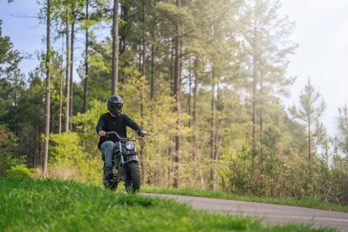 Greenworks electric mini-bike — rider on a forest trail through tall trees