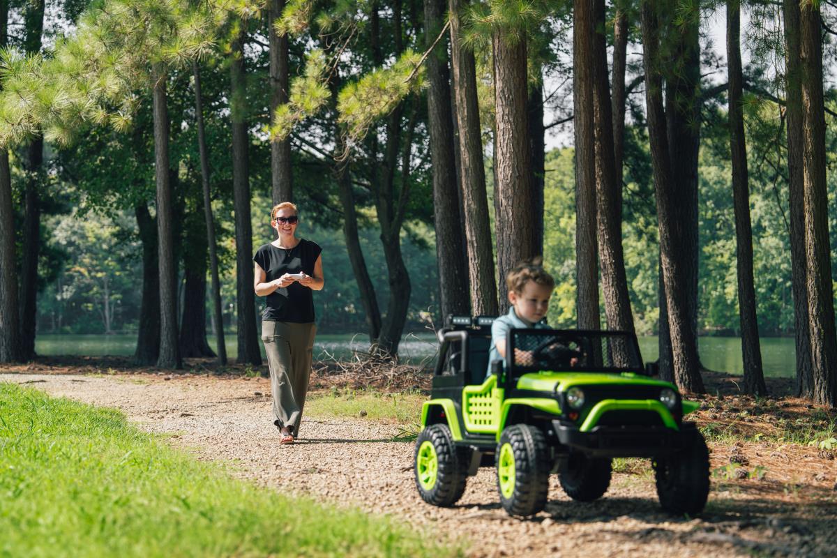 Greenworks kids ride-on car — child driving on a forest trail with parent nearby